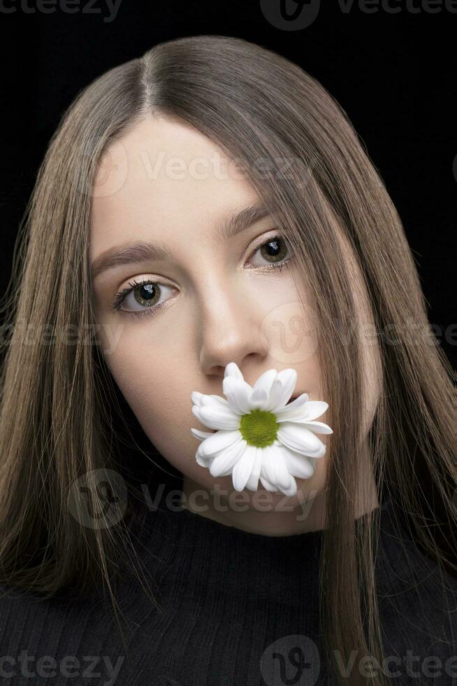 A beautiful girl with natural beauty holds a white flower in her mouth. Young girl with a white chrysanthemum. photo