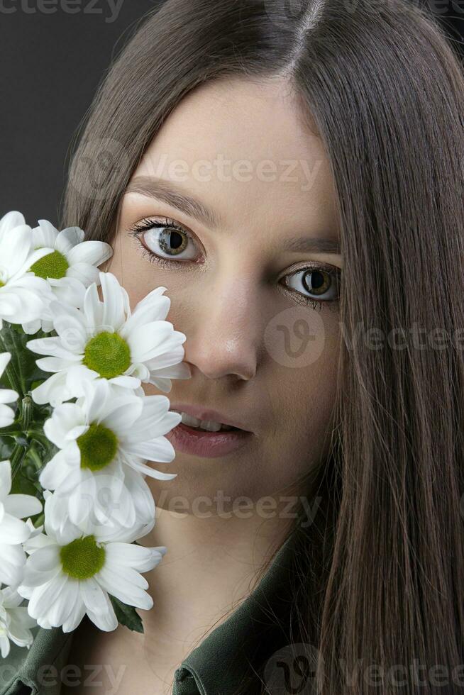 A beautiful young girl with natural beauty with long smooth hair holds a bouquet of white chrysanthemums. photo