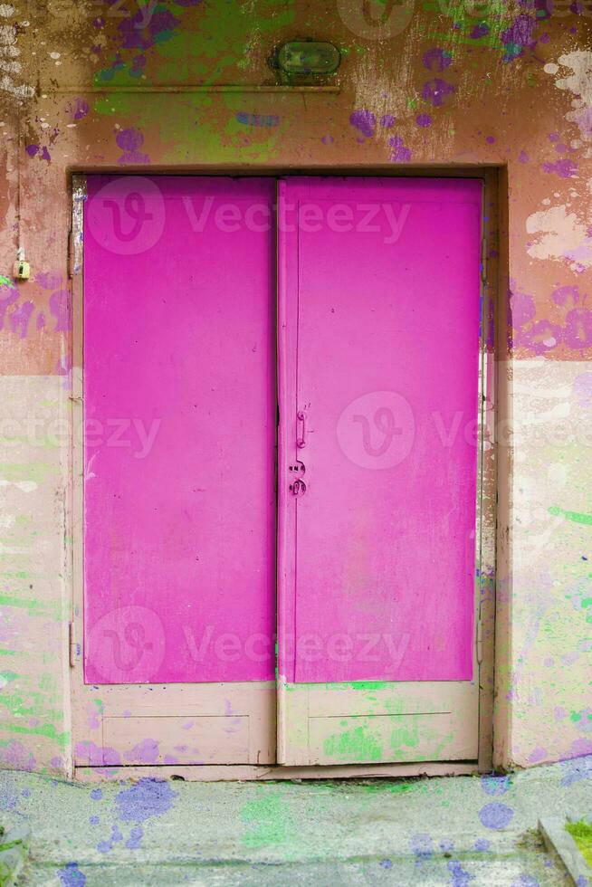 The old wooden doors are bright pink and the wall is covered with paint. photo