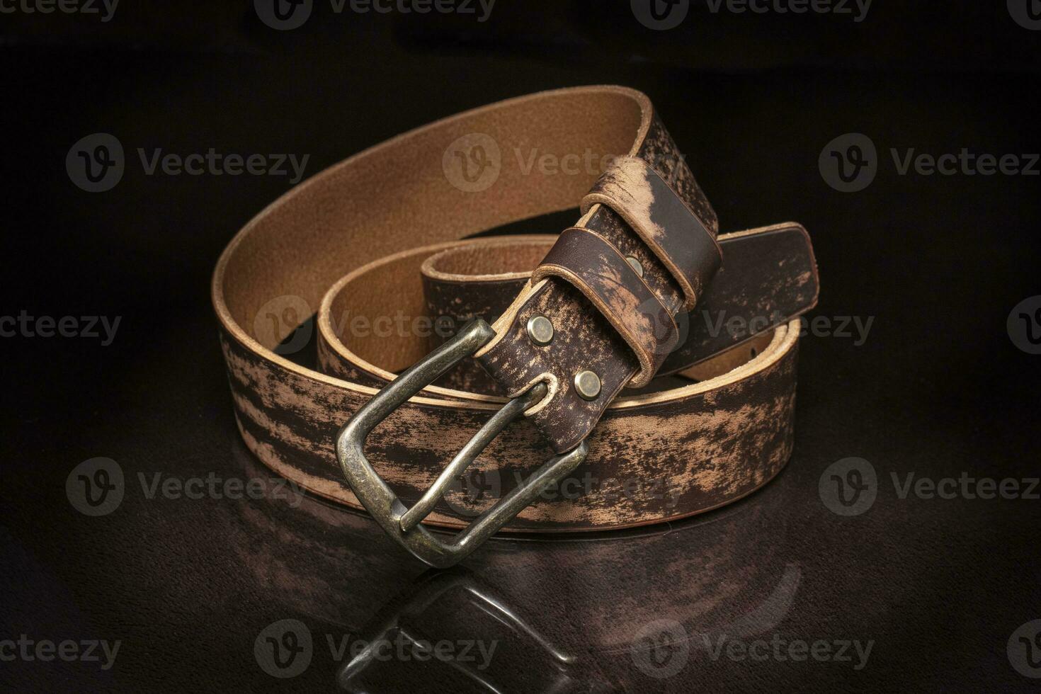 Brown leather belt with scuffs and a metal buckle on a dark background. photo