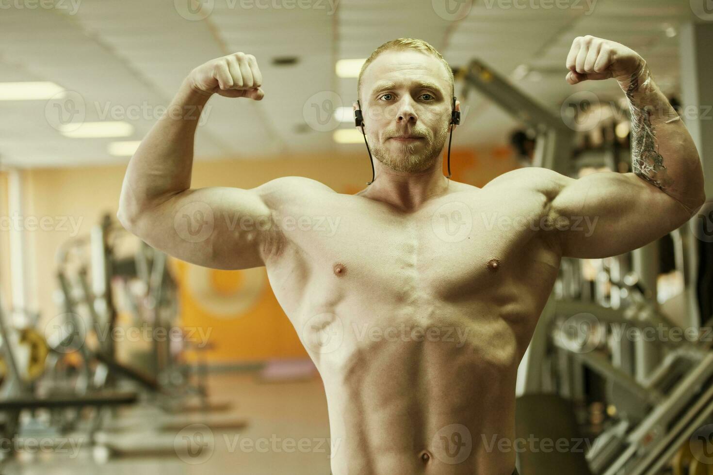 A handsome young man of athletic physique shows biceps on the background of the gym. photo
