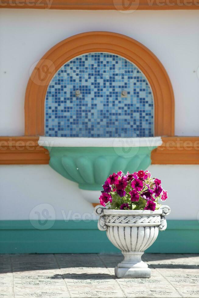 An earthenware vase with petunia flowers stands by the church washstand. Beautiful flowers in the street. photo