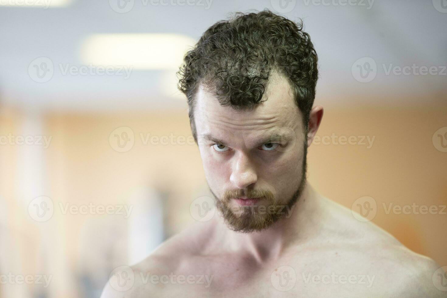 un joven hombre con un barba mira fuera desde debajo su Cejas. foto