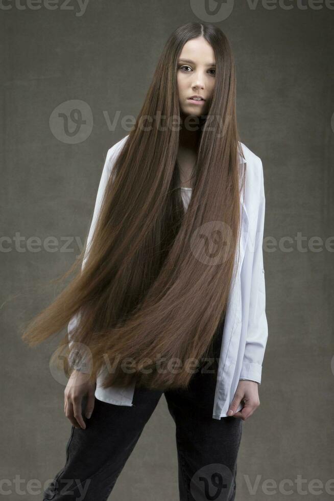 Beautiful brunette girl with very long and smooth hair on a gray background. Luxurious hair length. photo