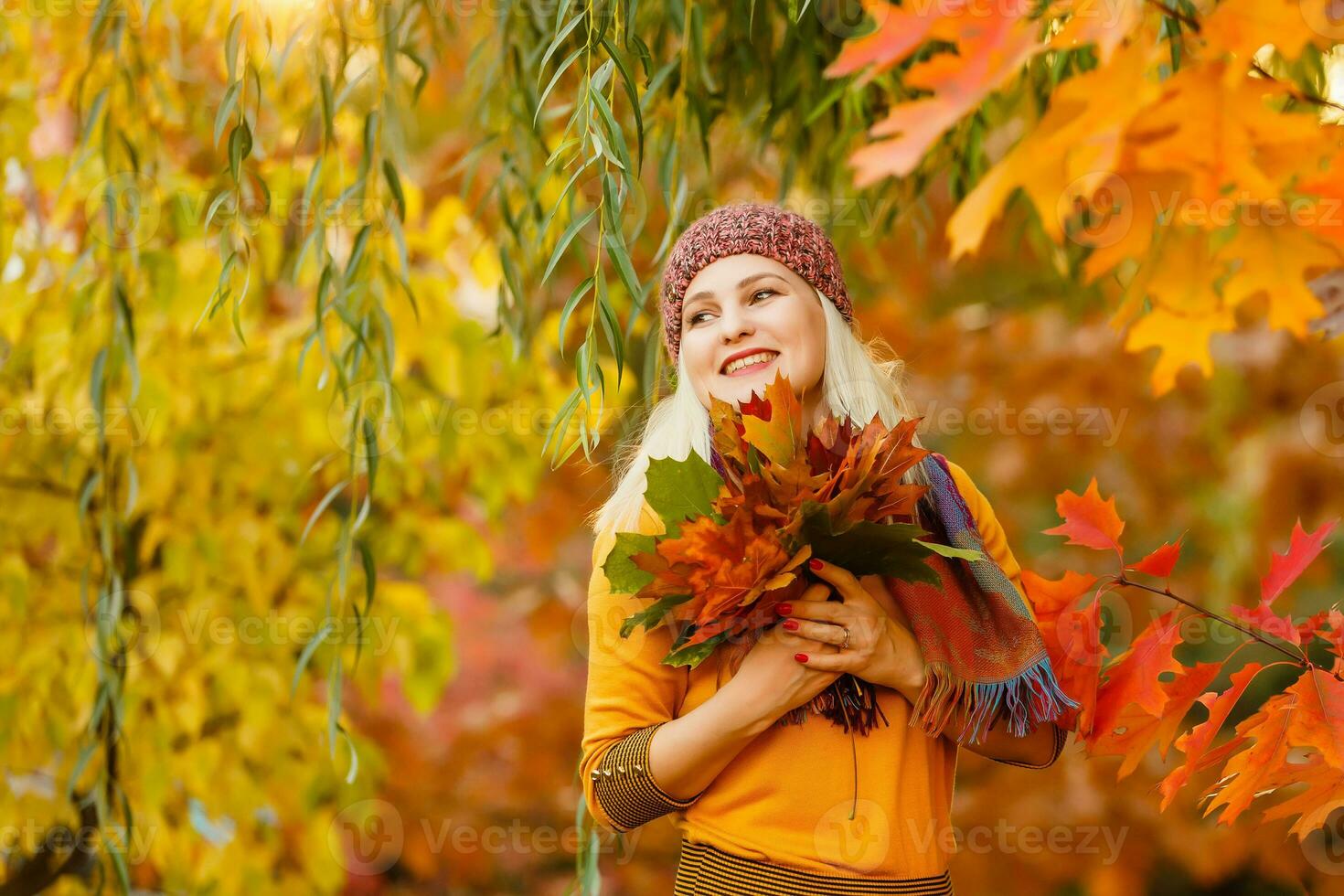 Portrait of cheerful young woman with autumn leafs in front of foliage making selfie photo