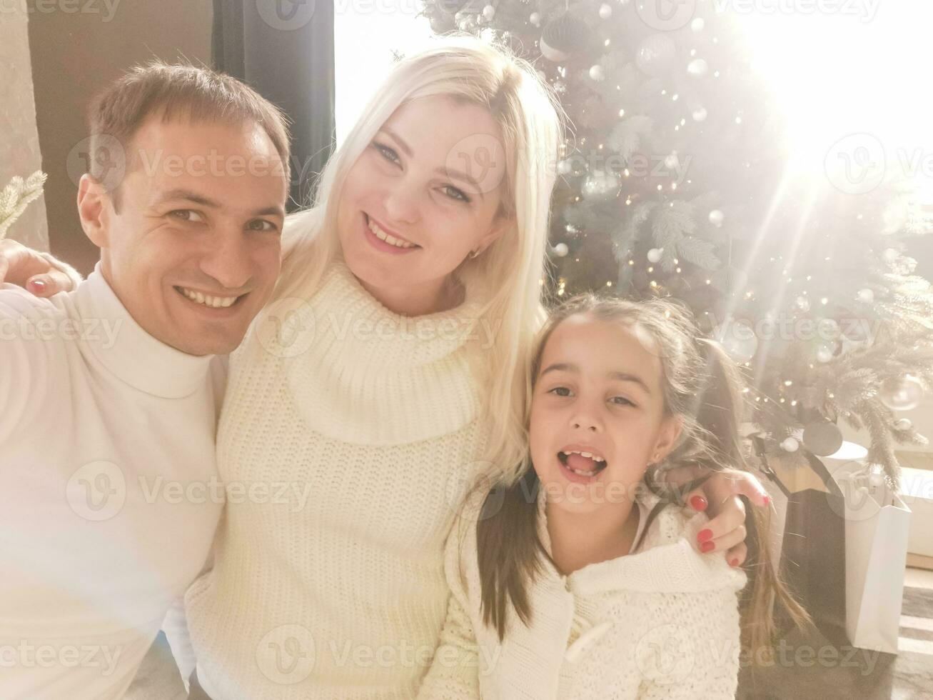 familia, vacaciones, tecnología y personas - sonriente madre, padre y pequeño niña haciendo selfie con cámara terminado vivo habitación y Navidad árbol antecedentes foto