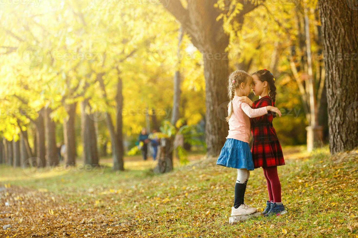 pequeño muchachas medida altura a cada otro en otoño parque foto