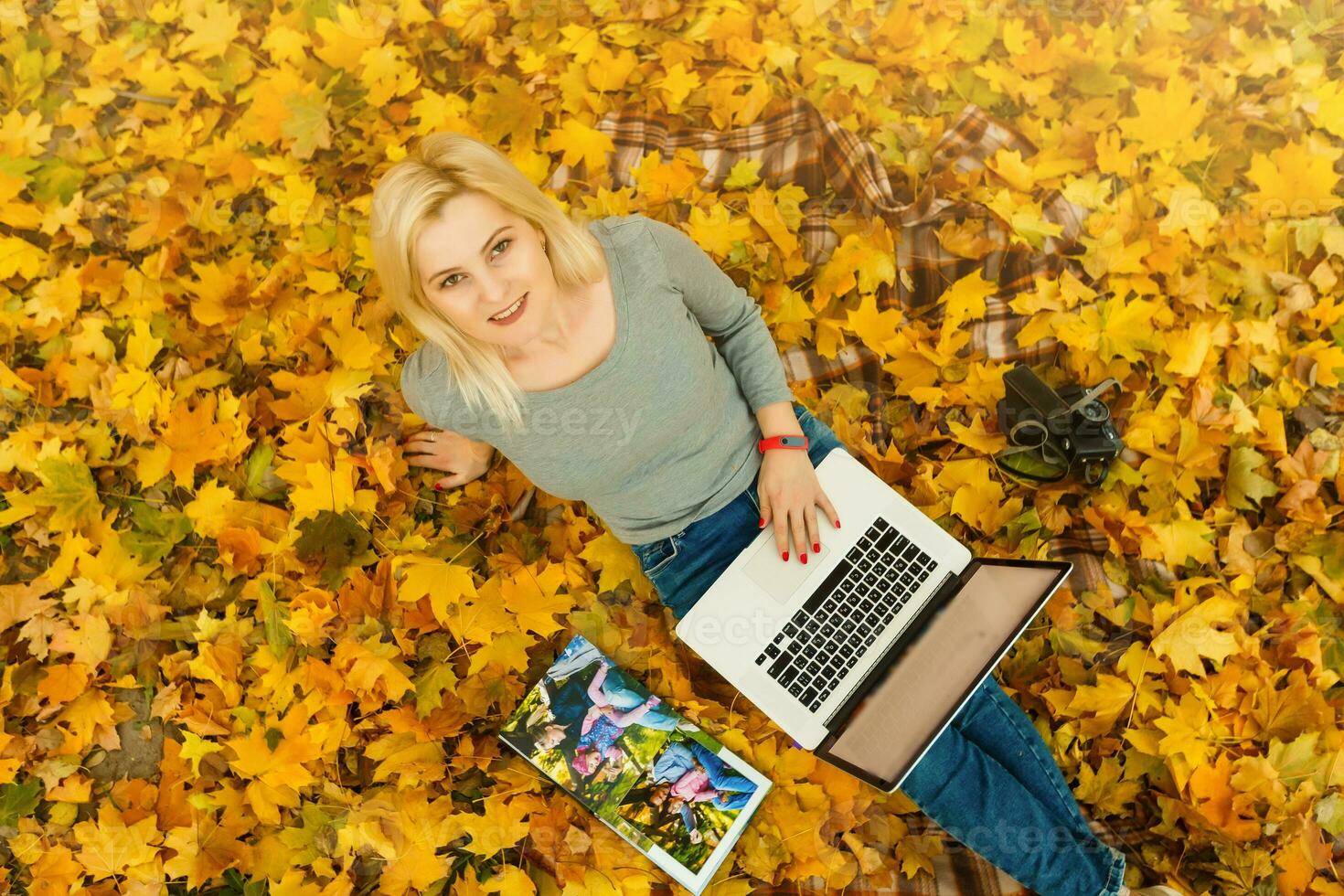 Cute woman with laptop in the autumn park. Beauty nature scene with colorful foliage background, yellow trees and leaves at fall season. Autumn outdoor lifestyle. Happy smiling woman on fall leaves photo