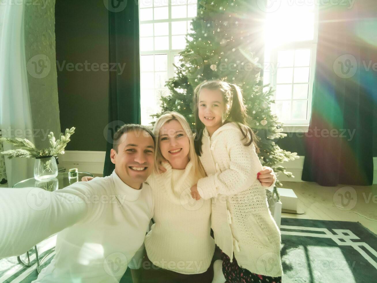 Christmas. Family. Technology. View on the smartphone. Dad, mom and daughter looking at camera and smiling while doing selfie photo