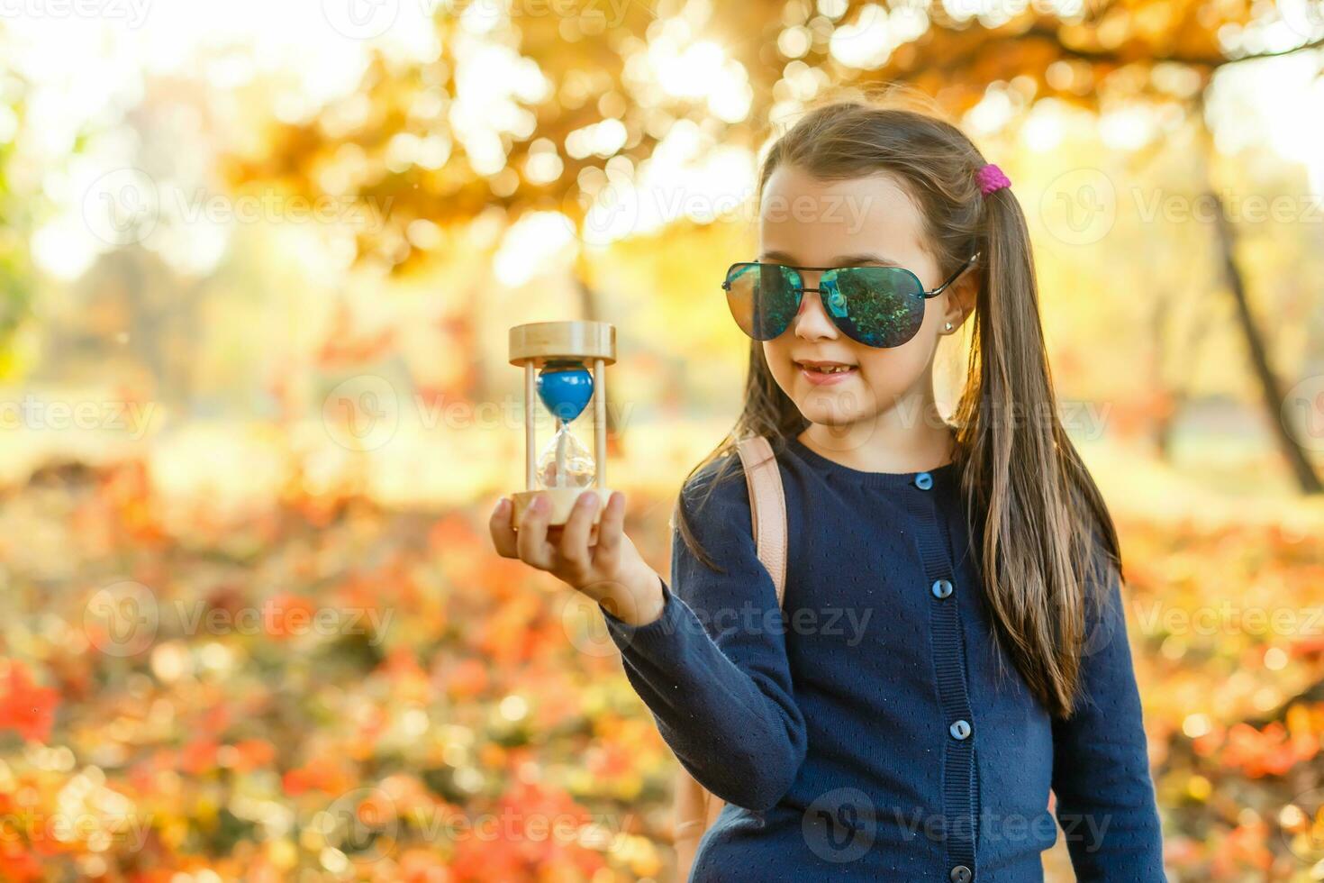little girl holds hourglass in autumn photo