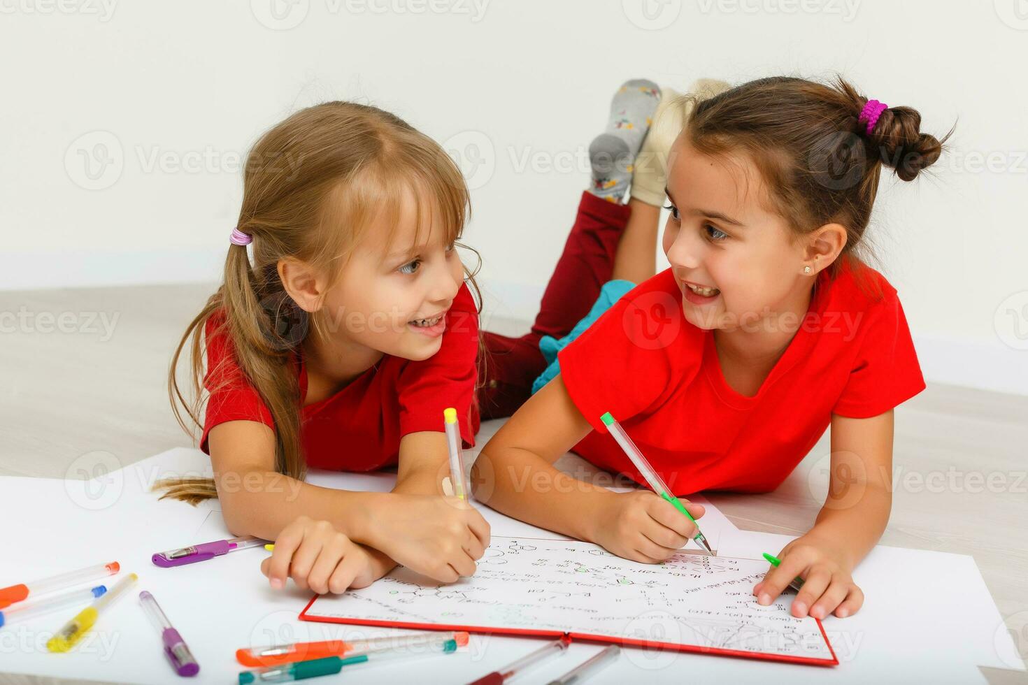 family, leisure and childhood concept - happy sisters lying on floor and drawing and doing homework at home photo