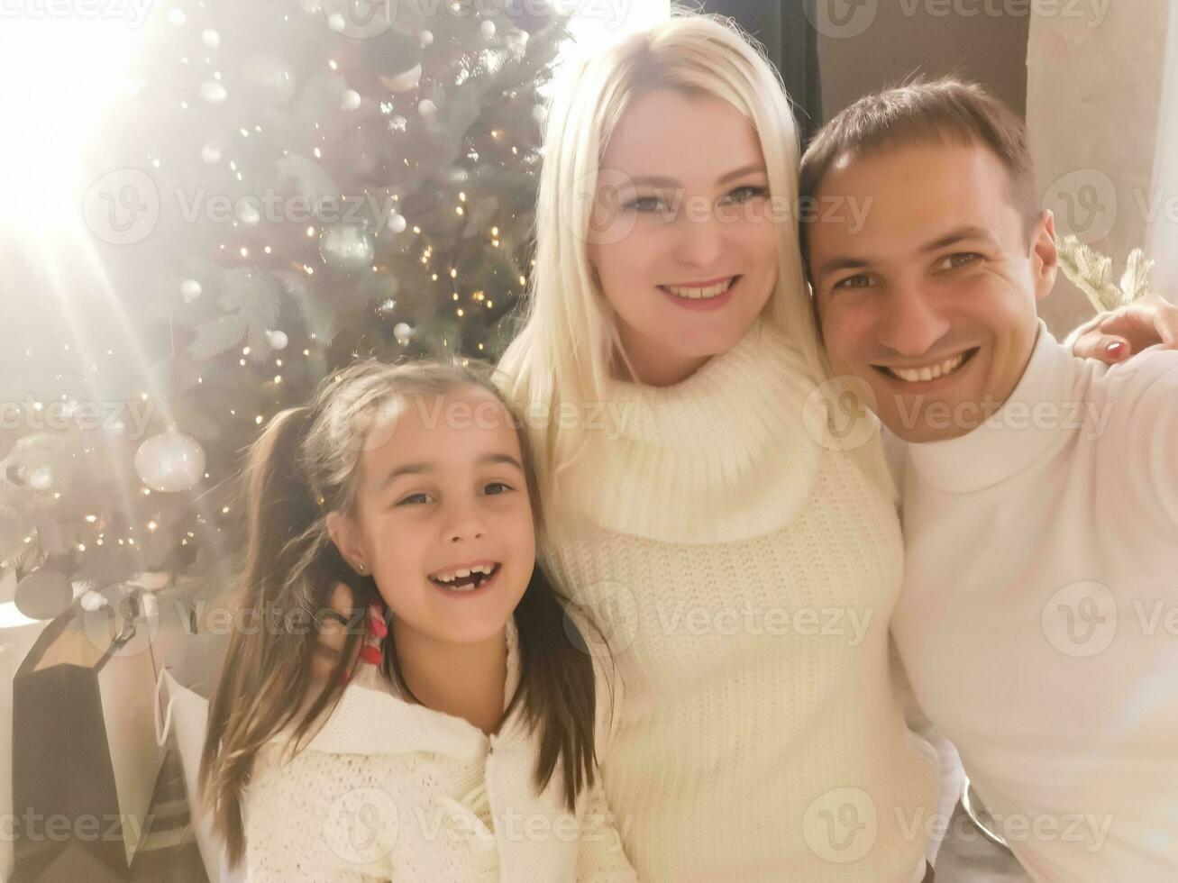 Christmas. Family. Technology. View on the smartphone. Dad, mom and daughter looking at camera and smiling while doing selfie photo