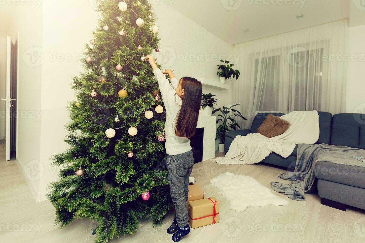 Portrait of a cute little girl dressed up as a reindeer Rudolf decorating a Christmas tree photo