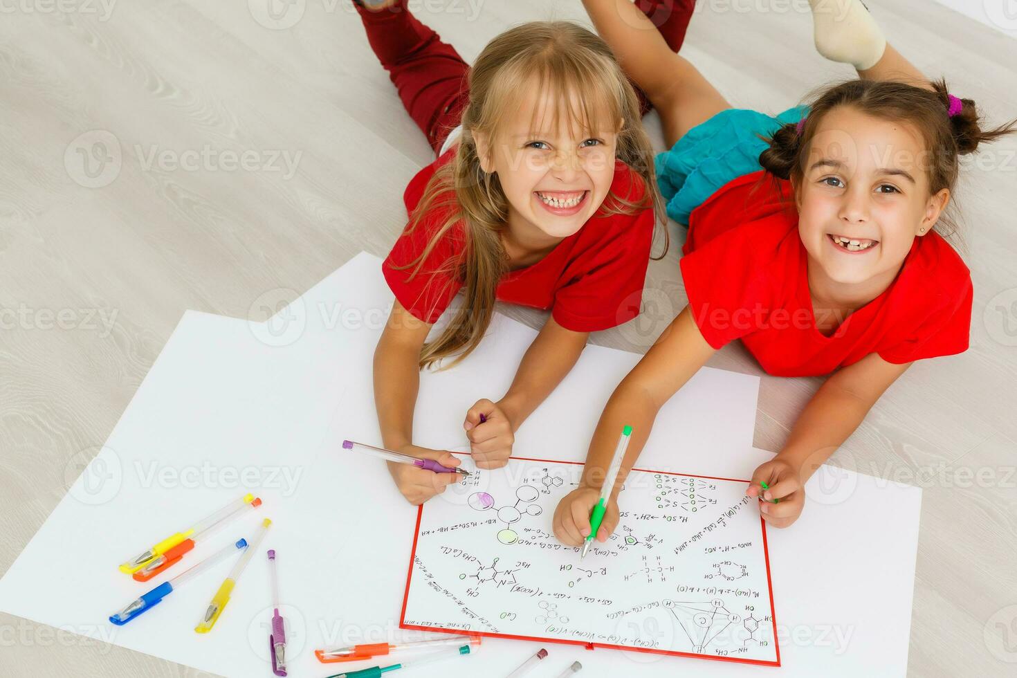 family, leisure and childhood concept - happy sisters lying on floor and drawing and doing homework at home photo