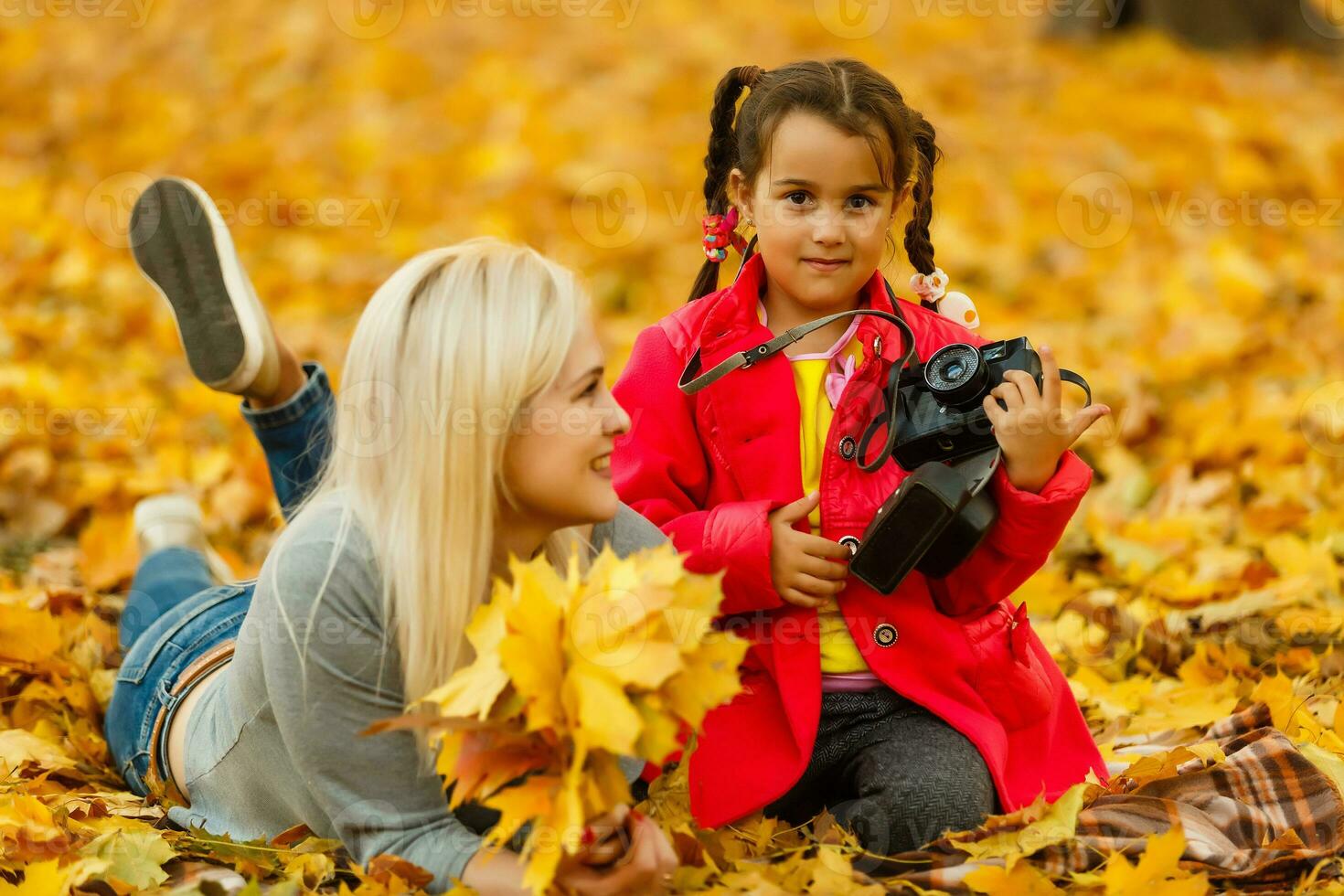 little girl plays with a camera in yellow leaves of autumn landscape photo