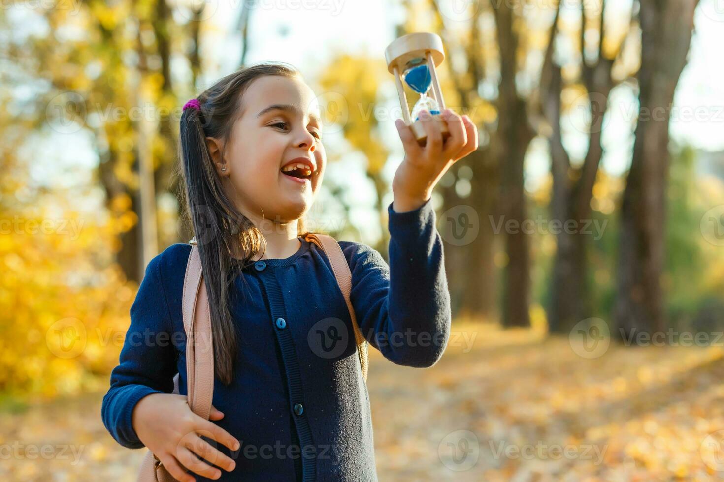 little girl schoolgirl holds hourglass in autumn photo