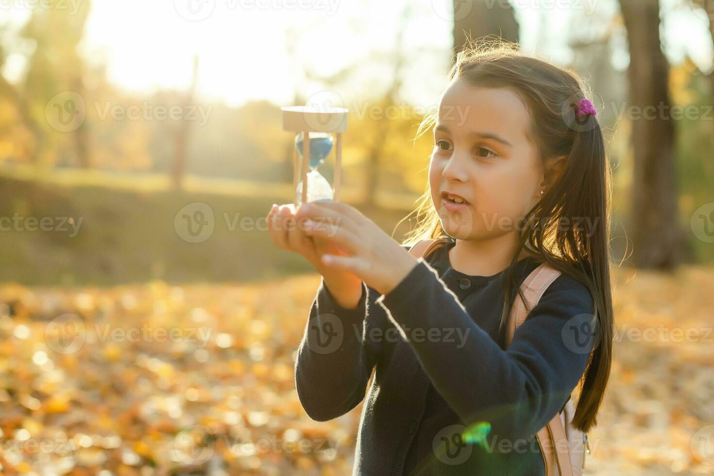 little girl schoolgirl holds hourglass in autumn photo