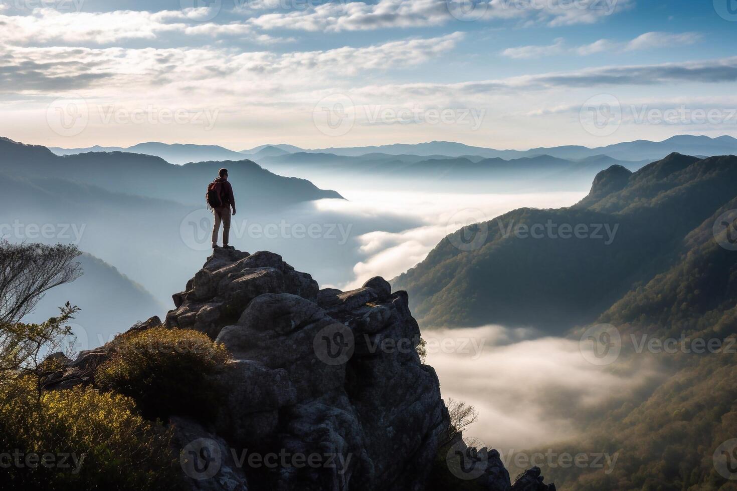 Back view of male manager carrying a suitcase while standing on the hills and looking at misty mountain. Shot at sunrise time photo