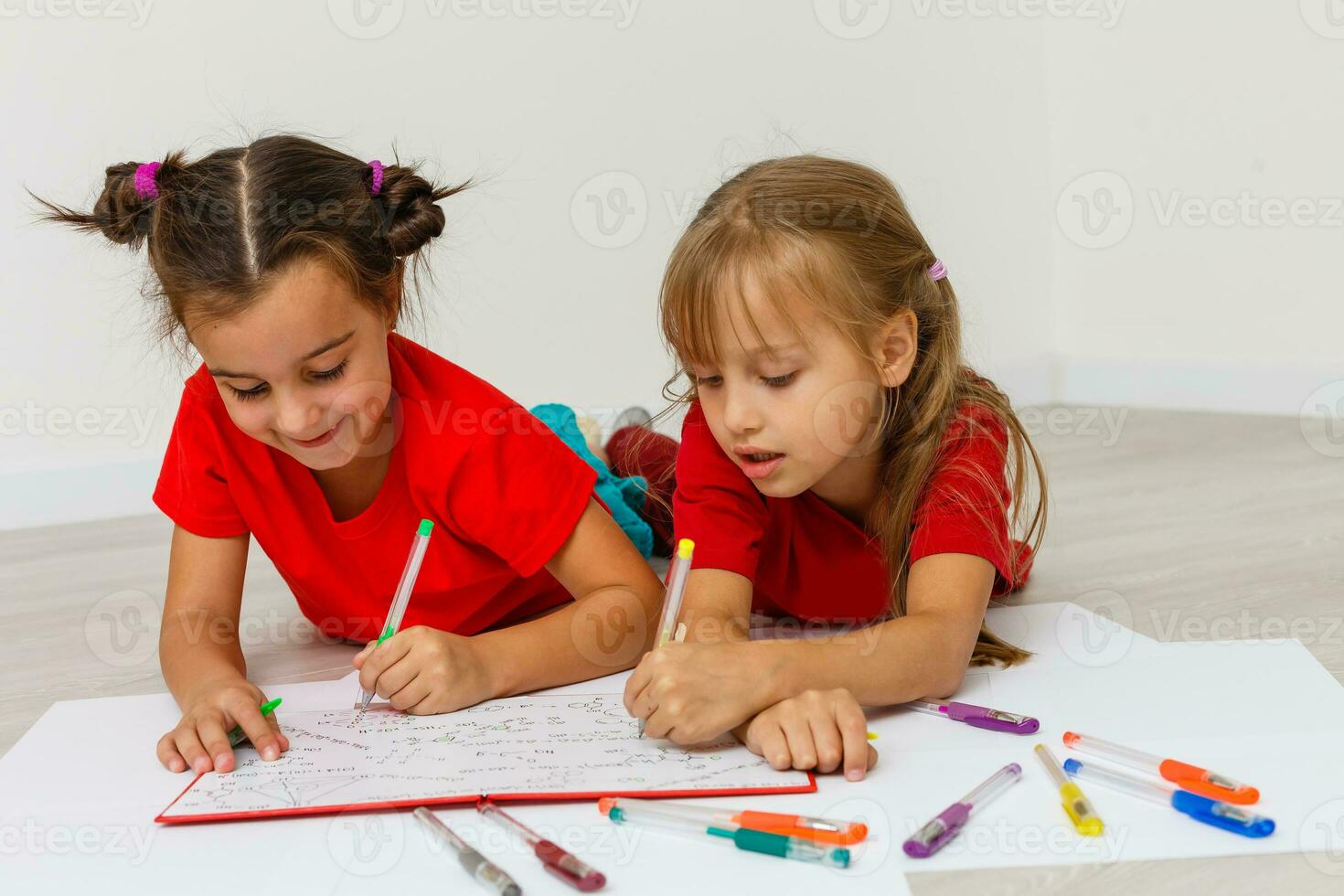 family, leisure and childhood concept - happy sisters lying on floor and drawing and doing homework at home photo