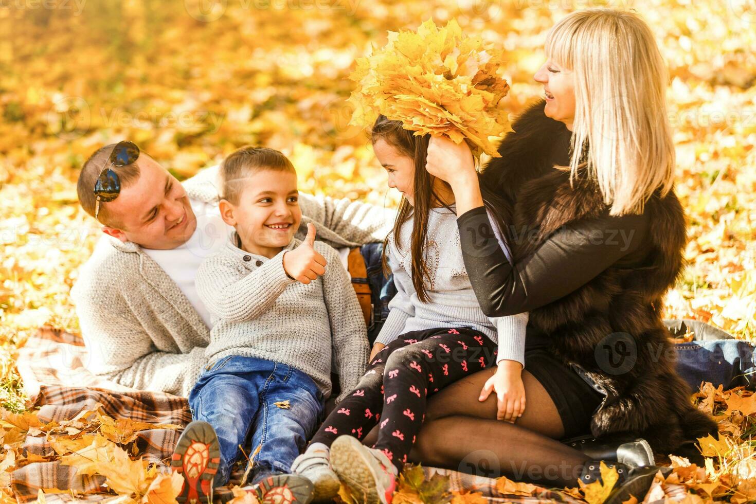 Smiling young family sitting in leaves on an autumns day photo