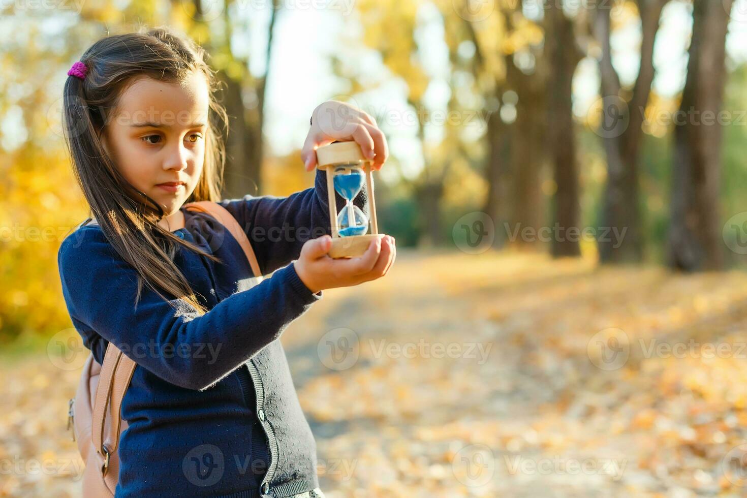 little girl with hourglass surrounded by autumn foliage photo