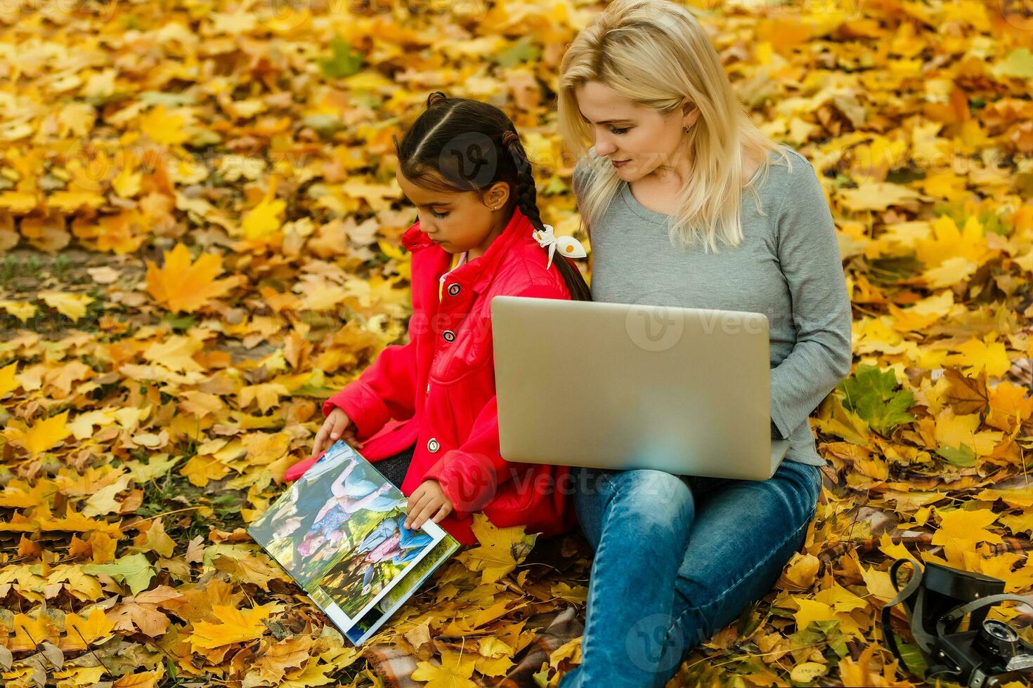 Happy smiling mother and child sits together looking on book or tablet pc in autumn park photo