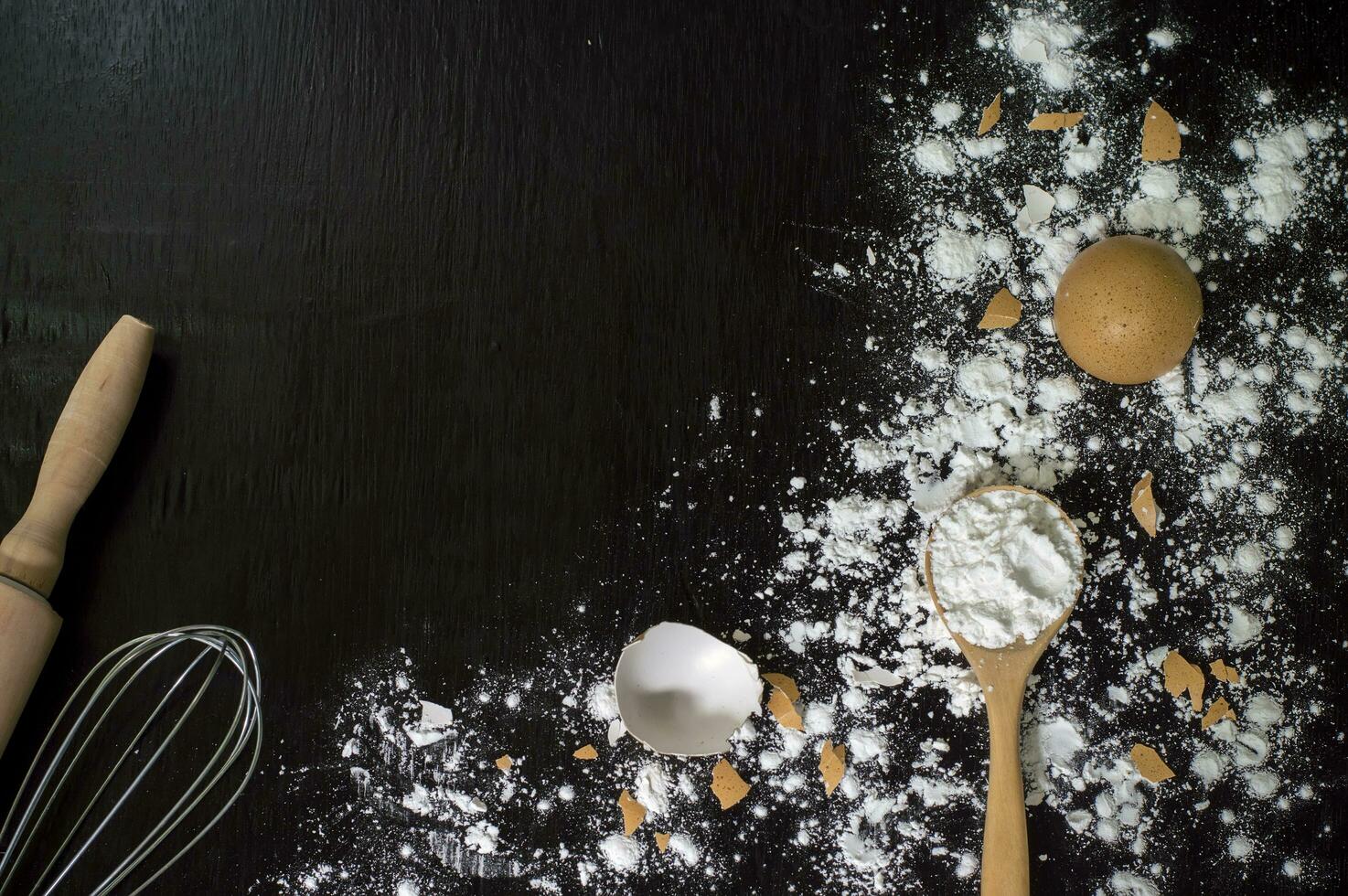 flour, eggs, whisk and wooden spoon on a black table photo