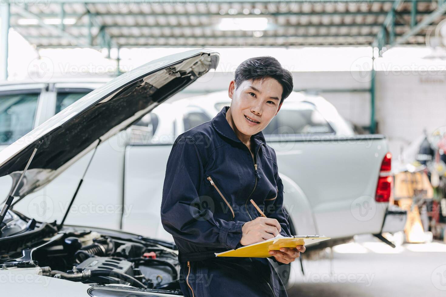 contento asiático mecánico joven masculino personal trabajador trabajando con coche motor frente capucha auto Servicio cheque Afinación motor en garaje foto