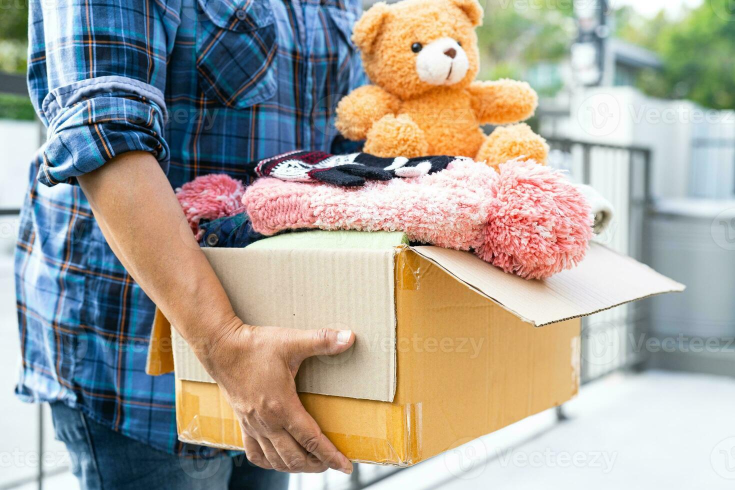 Volunteer woman provide clothing donation box with used clothes and doll to support help for refugee, homeless or poor people in the world. photo