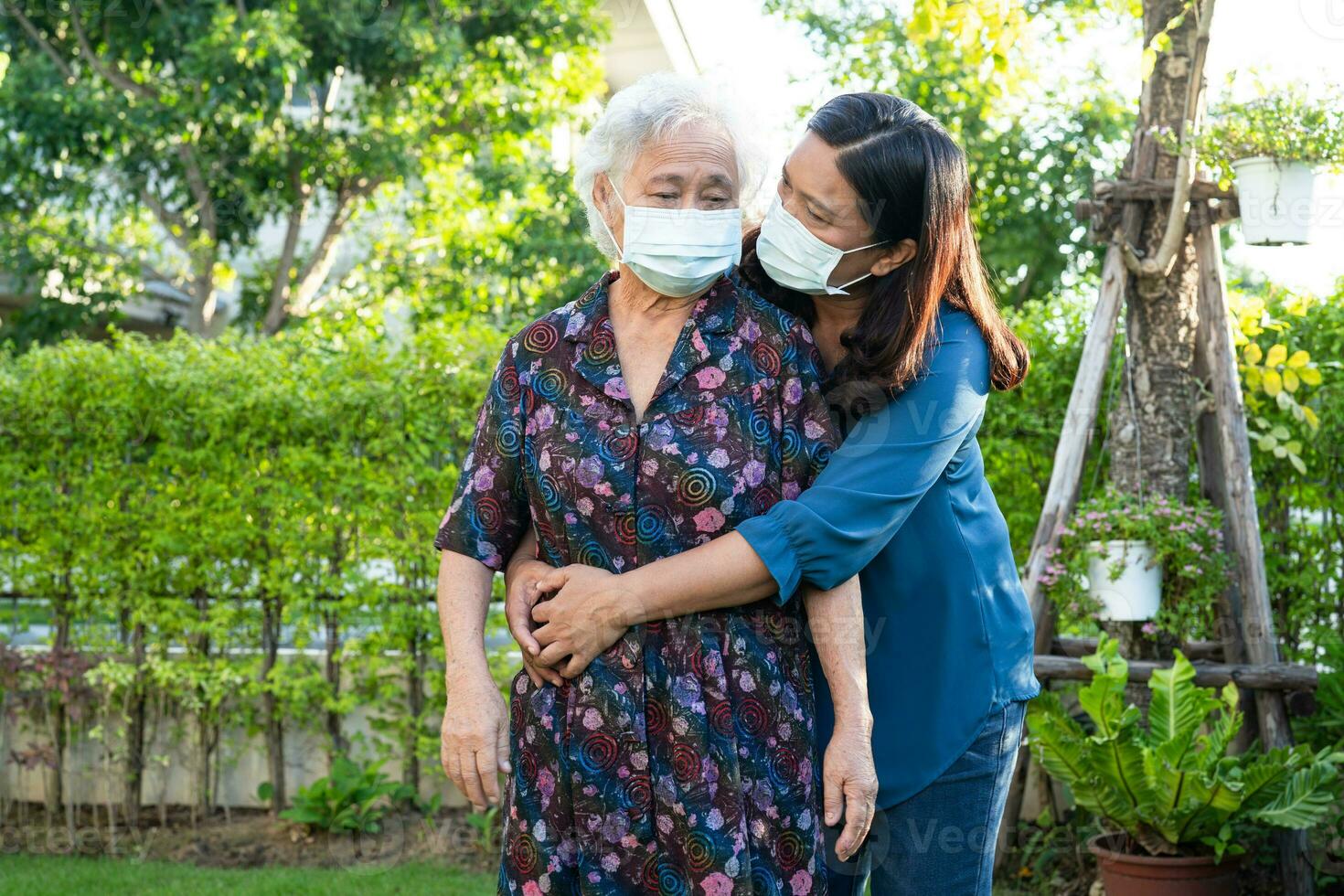Caregiver help Asian elderly woman patient wearing face mask walk in park, healthy strong medical concept. photo
