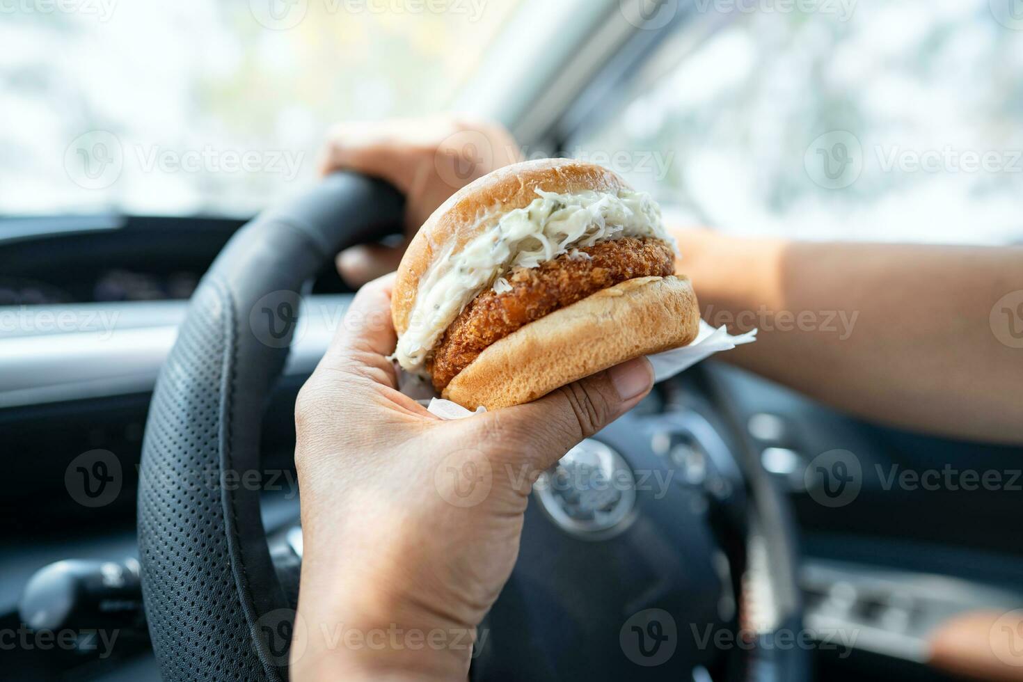 Asian lady holding hamburger to eat in car, dangerous and risk an accident. photo
