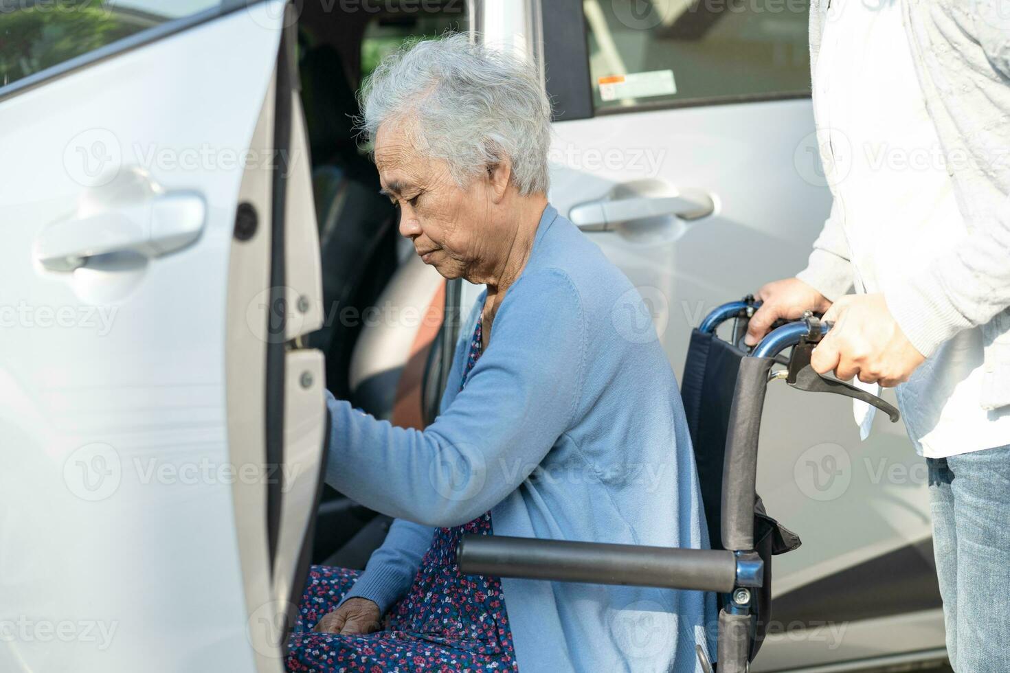 Caregiver help and support asian elderly woman sitting on wheelchair prepare get to her car to travel in holiday. photo