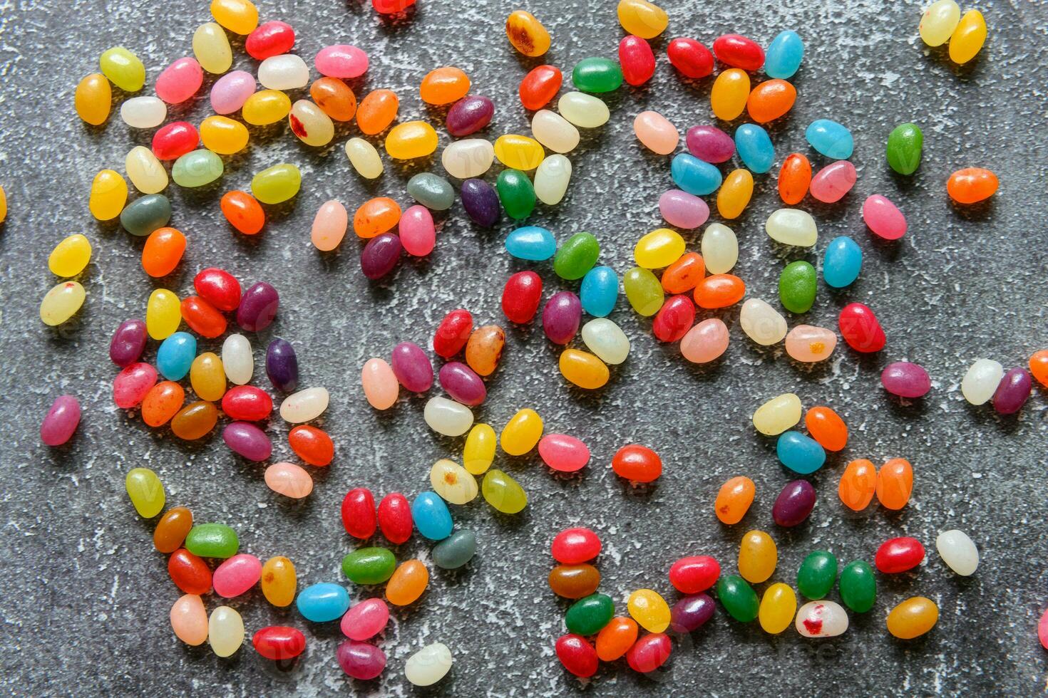 Big pile of colorful jellybeans spread out on rustic grey background photo