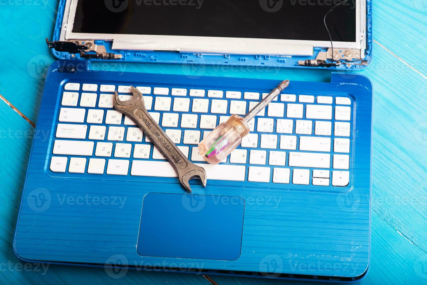 Wizard repairs laptop with tools and hands on the blue wooding table. top view. wrench and screwdriver on the keyboard photo