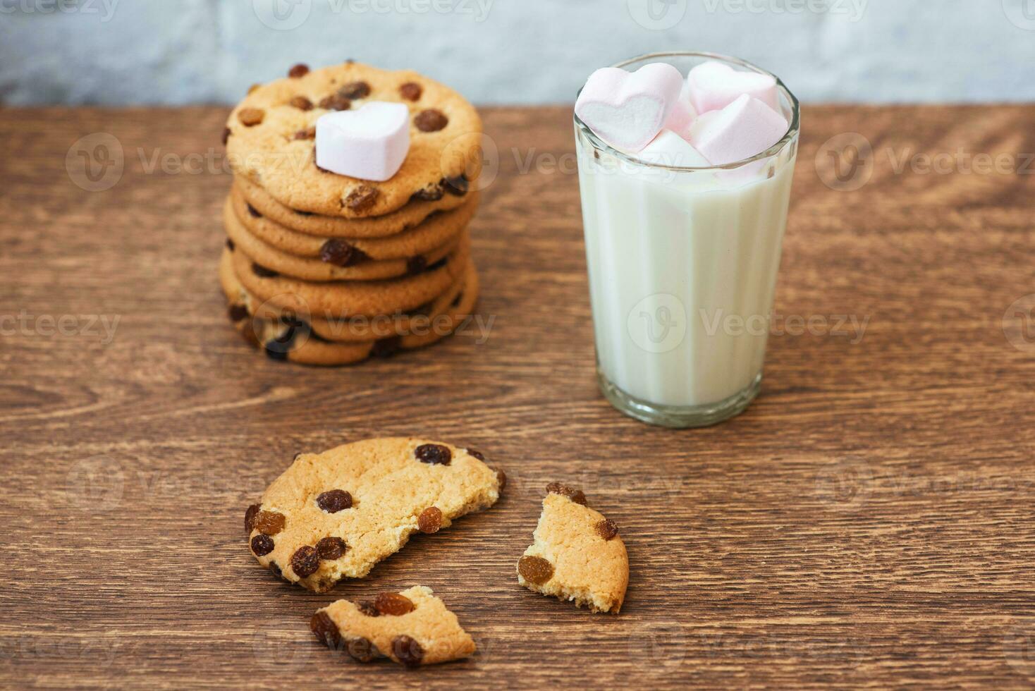 Fragrant, tasty, homemade cookies with raisins, marshmallow in a heart form and a glass of fresh milk on the table photo