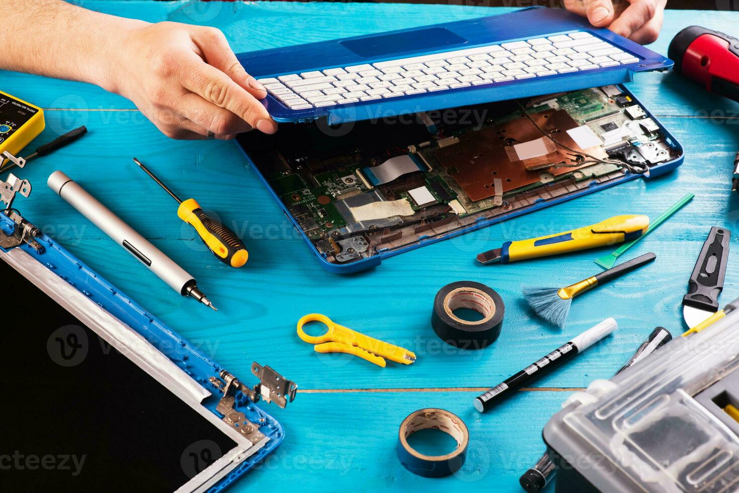 el asistente repara la computadora portátil con herramientas y manos en la mesa de madera azul. vista superior foto