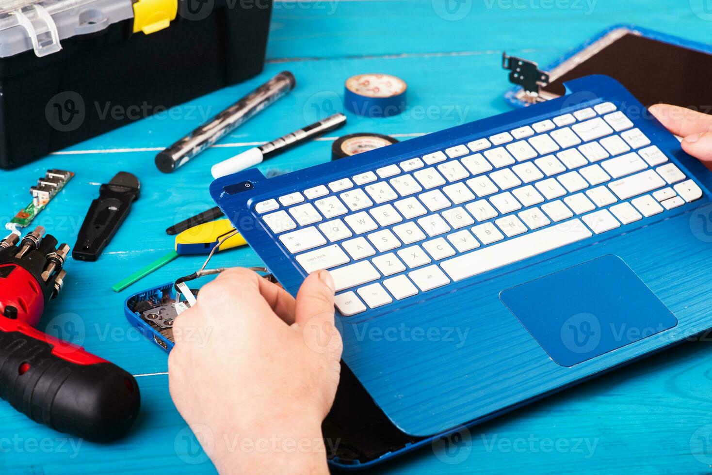 Wizard repairs laptop with tools and hands on the blue wooding table. top view photo