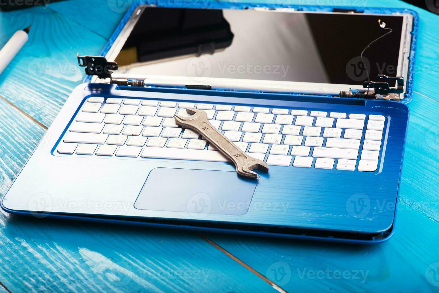 Wizard repairs laptop with tools and hands on the blue wooding table. top view. wrench and screwdriver on the keyboard photo