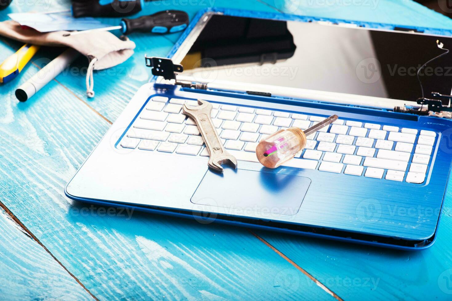 Wizard repairs laptop with tools and hands on the blue wooding table. top view. wrench and screwdriver on the keyboard photo