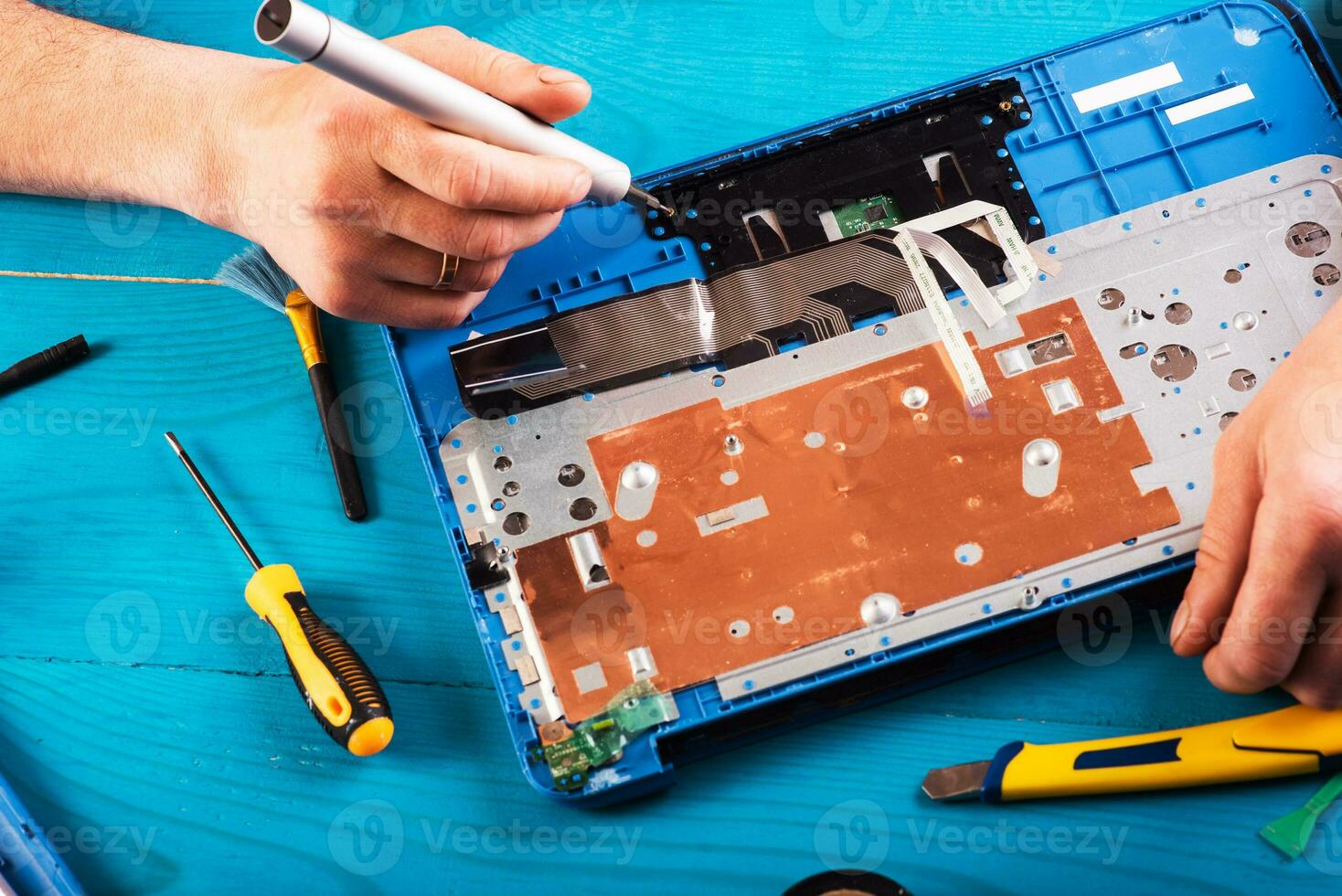 el asistente repara la computadora portátil con herramientas y manos en la mesa de madera azul. vista superior foto