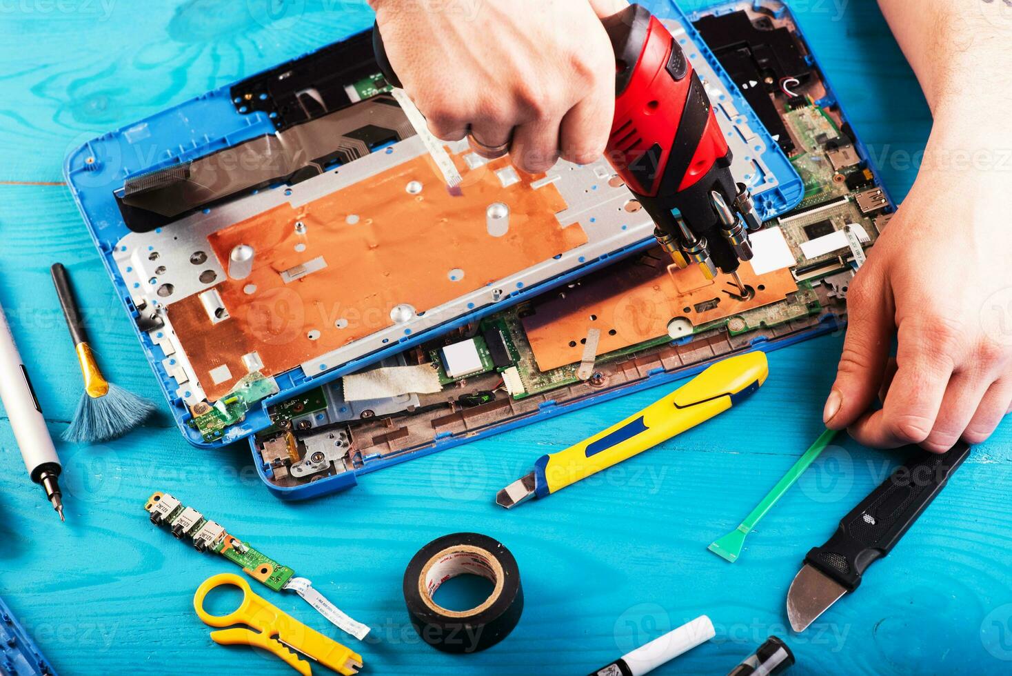 el asistente repara la computadora portátil con herramientas y manos en la mesa de madera azul. vista superior foto