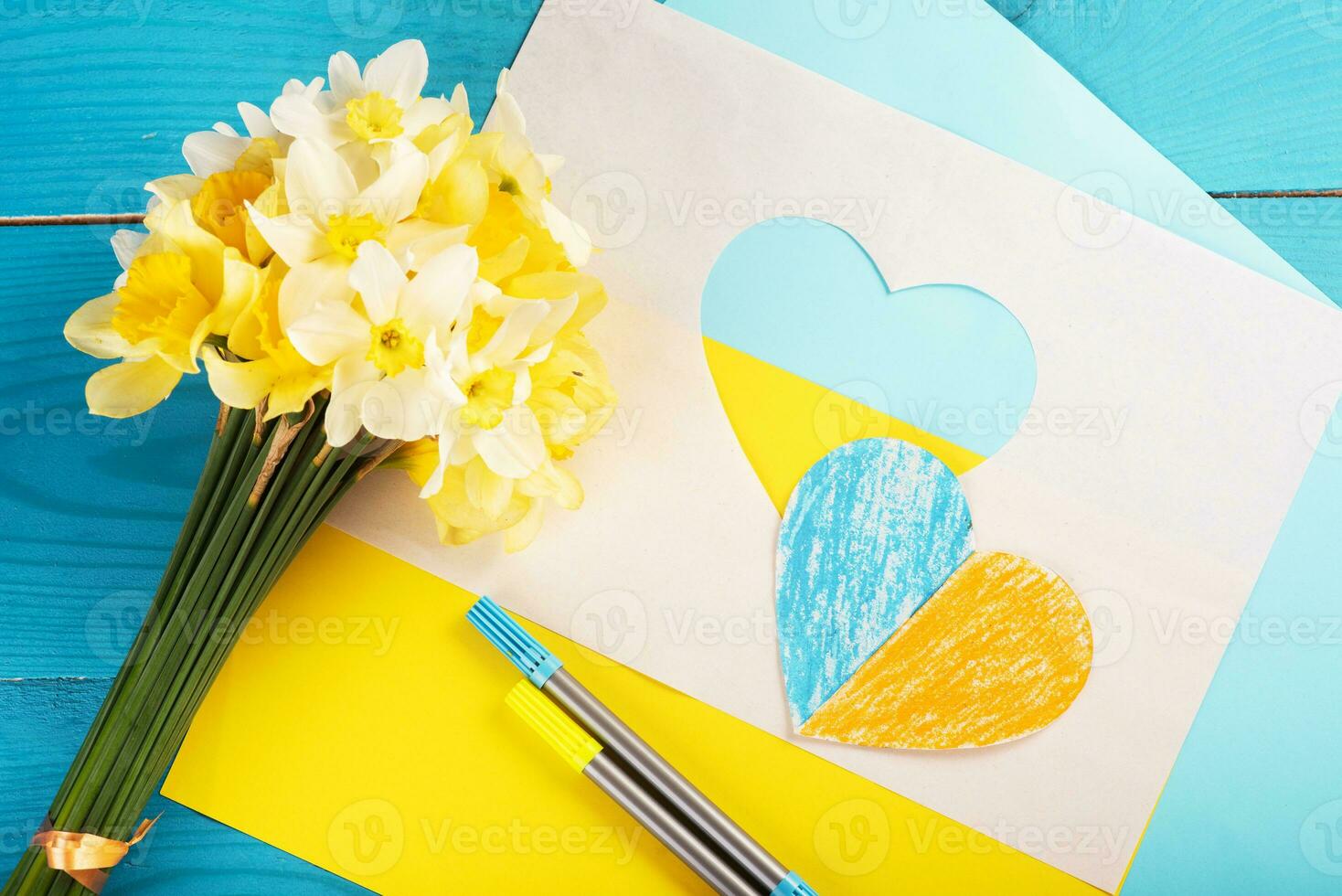 heart cut out of paper and painted in blue and yellow colors and yellow spring flowers on wooding back. Creativity photo