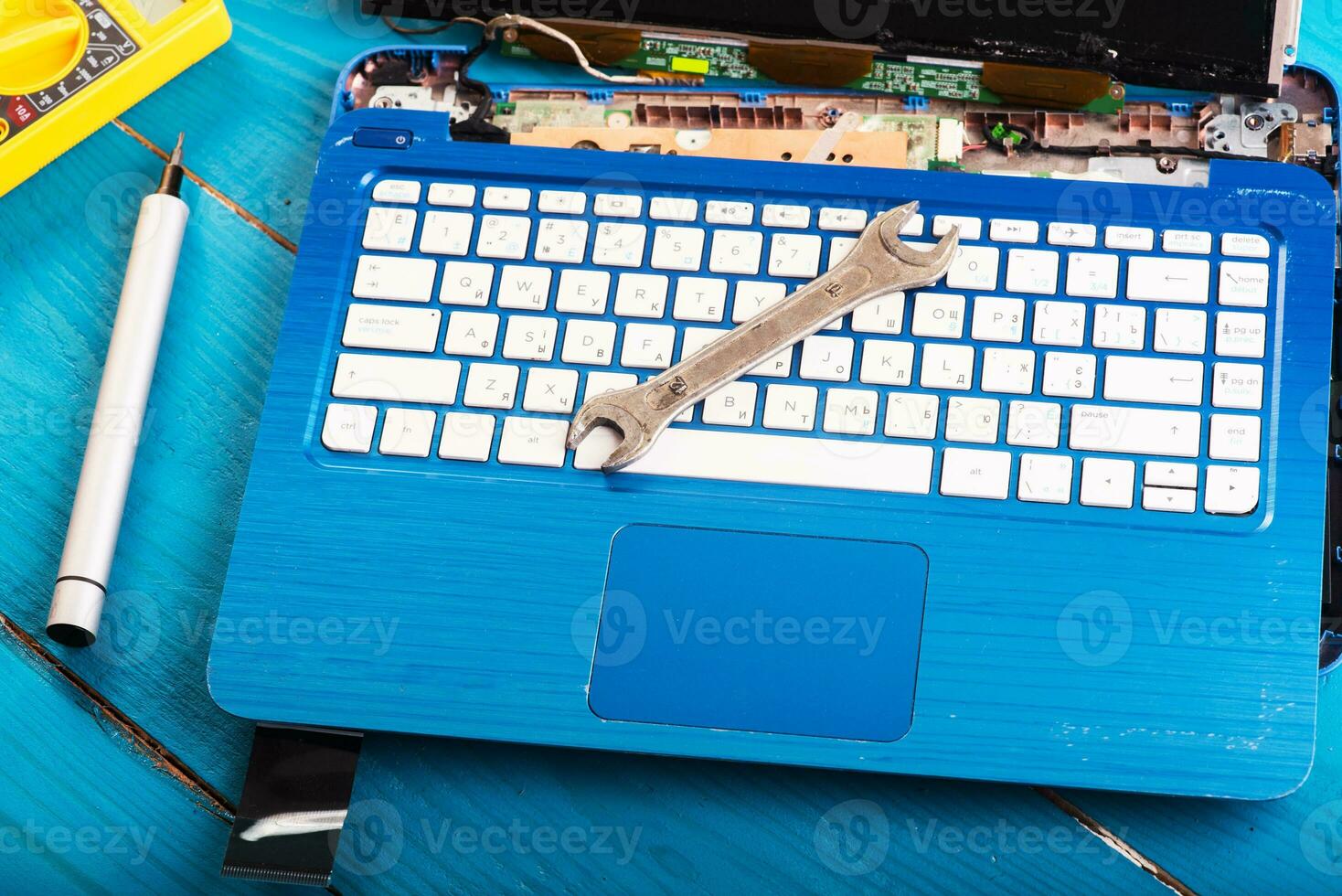 Wizard repairs laptop with tools and hands on the blue wooding table. top view. wrench and screwdriver on the keyboard photo