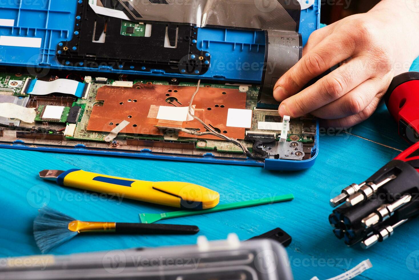 el asistente repara la computadora portátil con herramientas y manos en la mesa de madera azul. vista superior foto