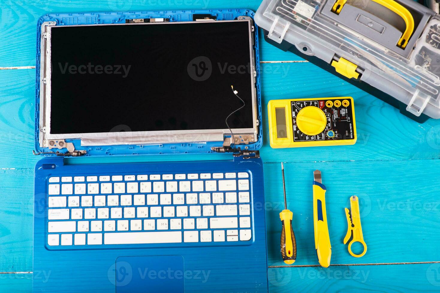 el asistente repara la computadora portátil con herramientas y manos en la mesa de madera azul. vista superior foto