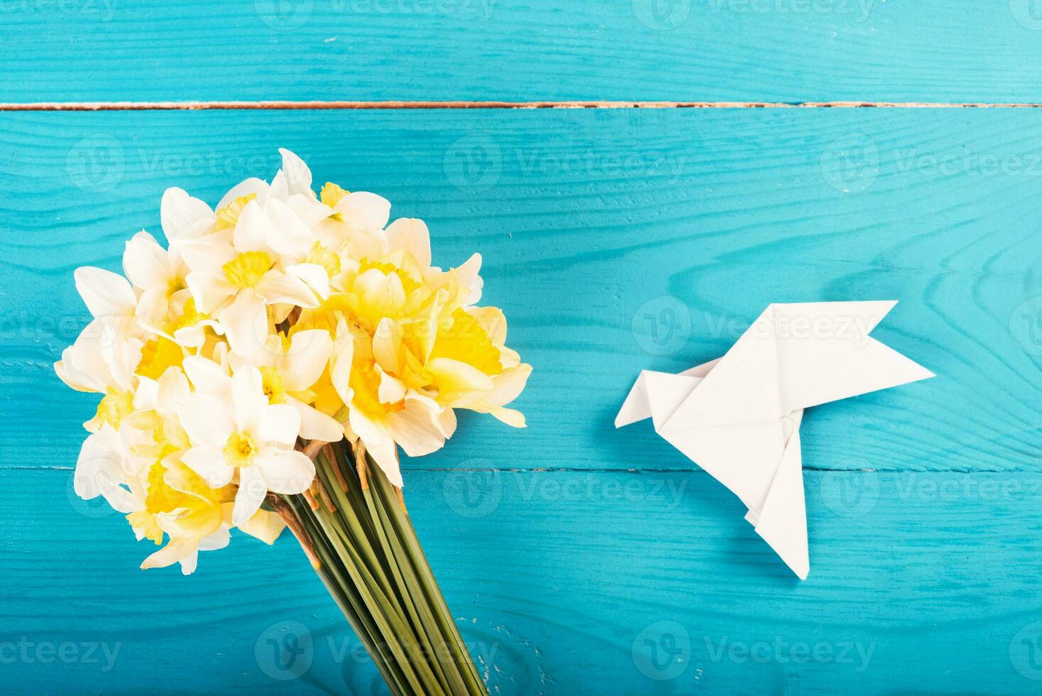 Yellow daffodils on a blue wooden background and white paper dove. Origami. View from above. Concept of Peace in Ukraine photo