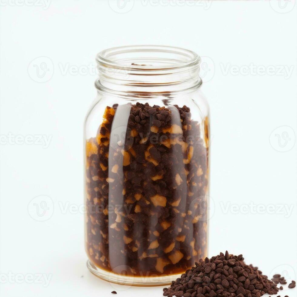 cocoa beans mixed with honey in a clear glass jar on a white background photo