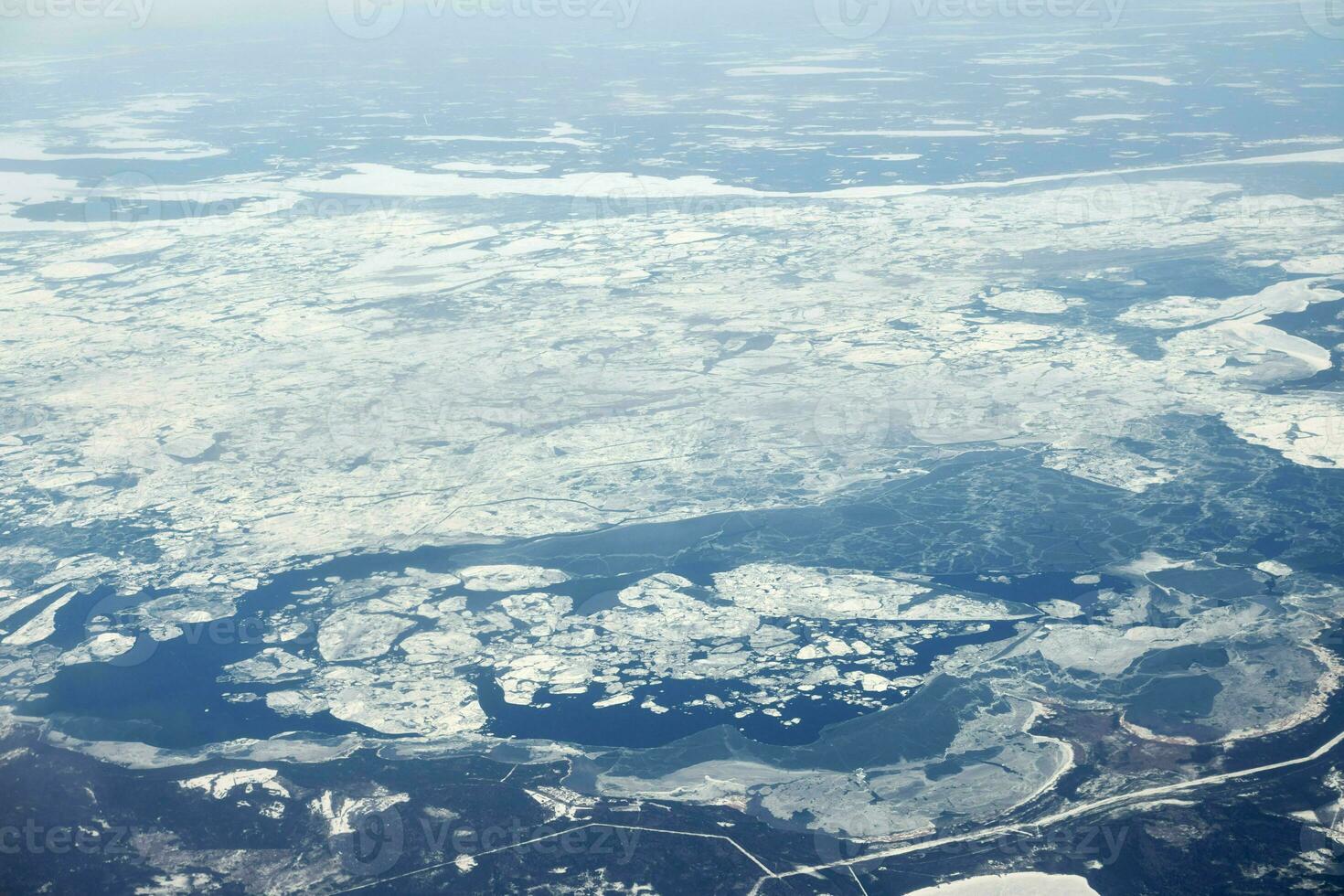 Aerial view from airplane window over clouds top to snow covered rivers, fields and roads photo