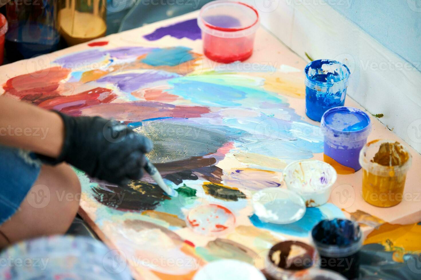 Artist hand in black gloves holds paint brush and choose color from colorful palette at art festival photo