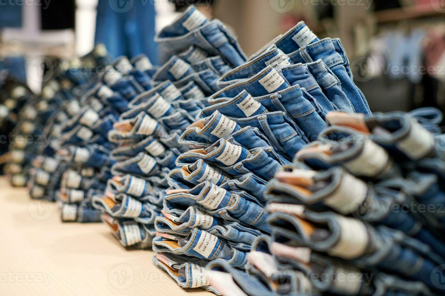 Denim jeans stack on wood table in clothing store, shopping photo